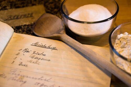 Handgeschriebenes Rezeptbuch mit alten Familienrezepten, daneben frische Zutaten zum Nachkochen.